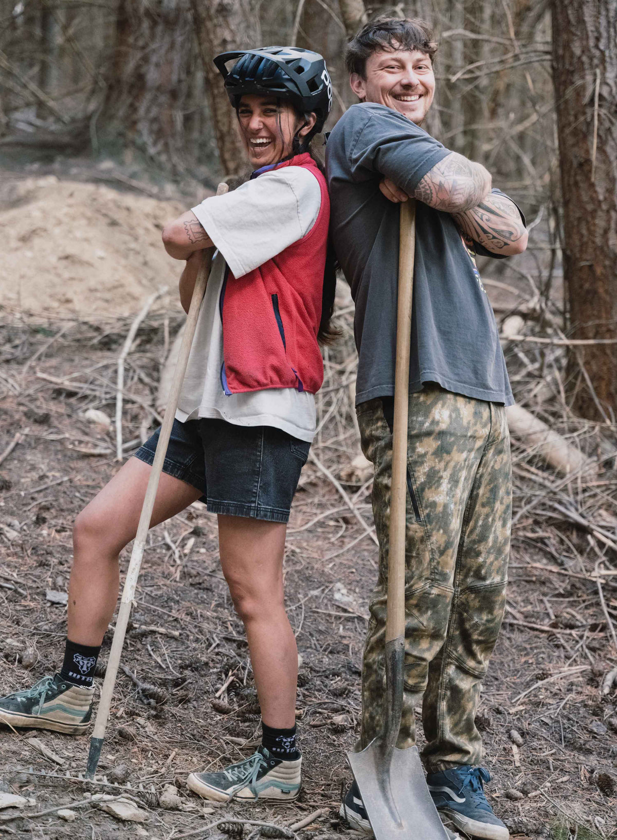 A man and woman standing back to back holding shovels