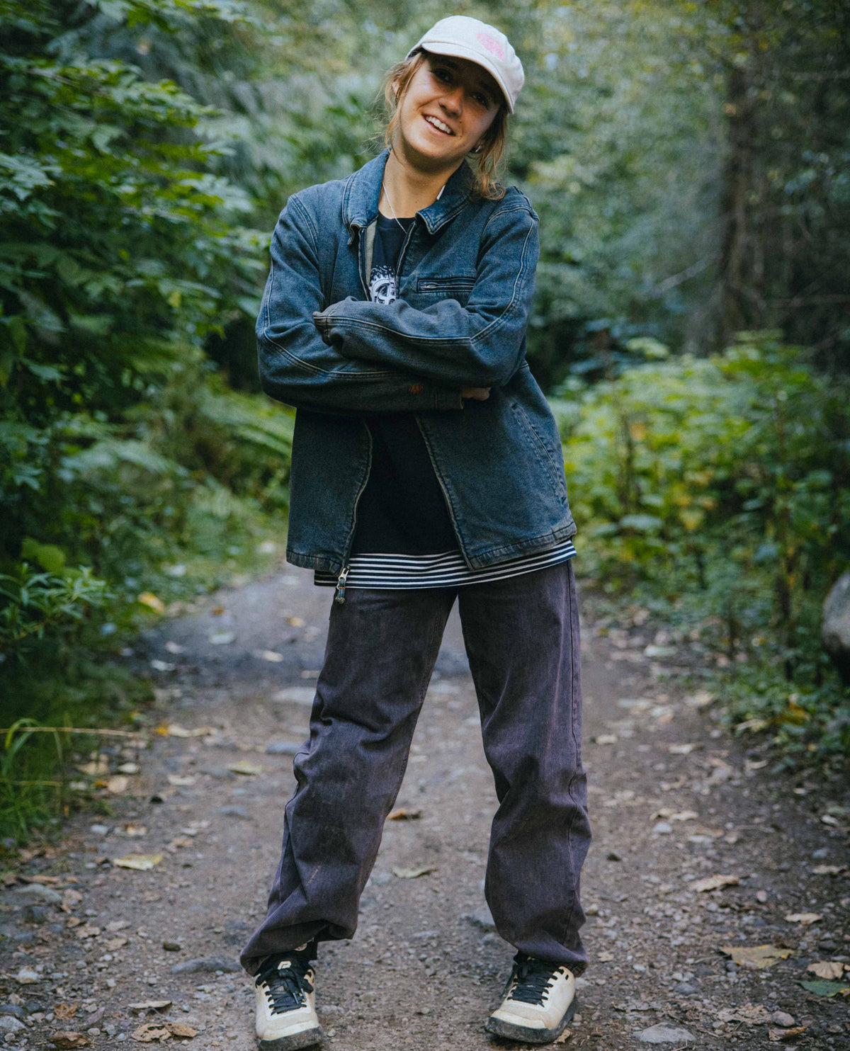 Person standing on a forest path wearing a blue jacket and gray pants.