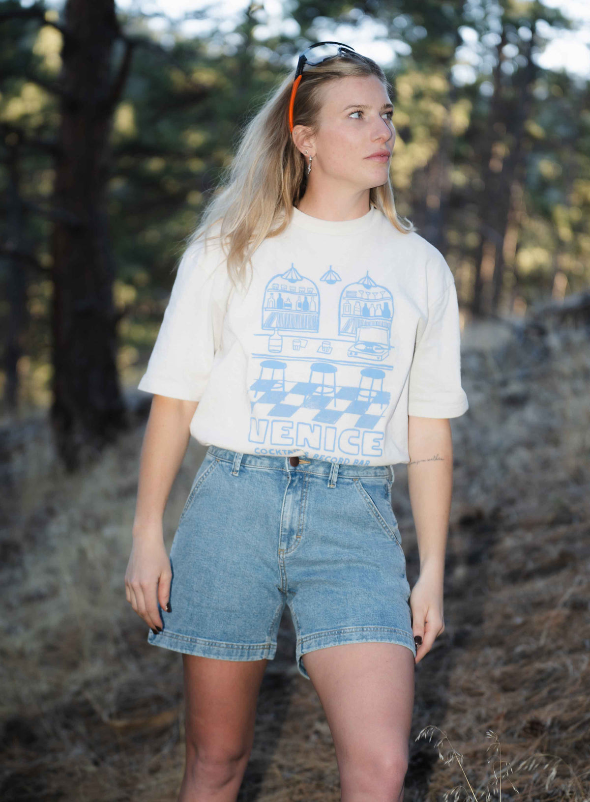 Blonde woman standing outside wearing blue shorts and white shirt