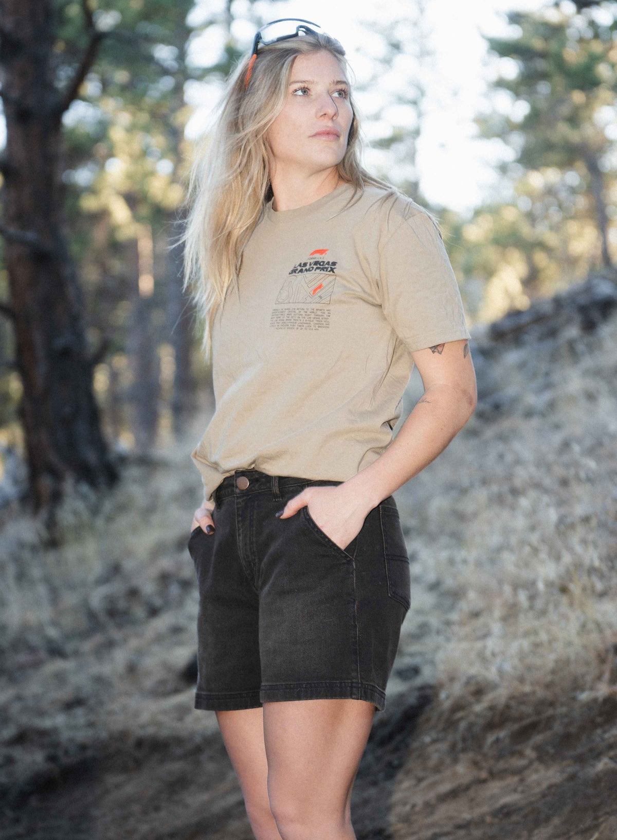 Blonde woman wearing tan shirt, black shorts, with hands in pockets standing outside