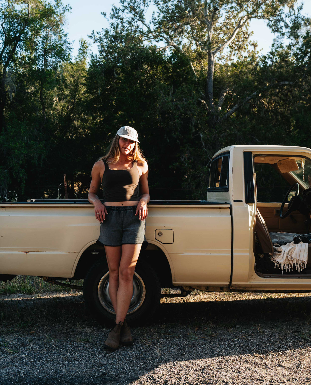 Girl leaning against a pickup truck with gray running shorts and blundstones