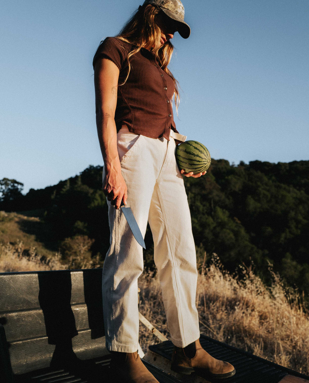 Girl wearing white flux pants holding a watermelon and a knife