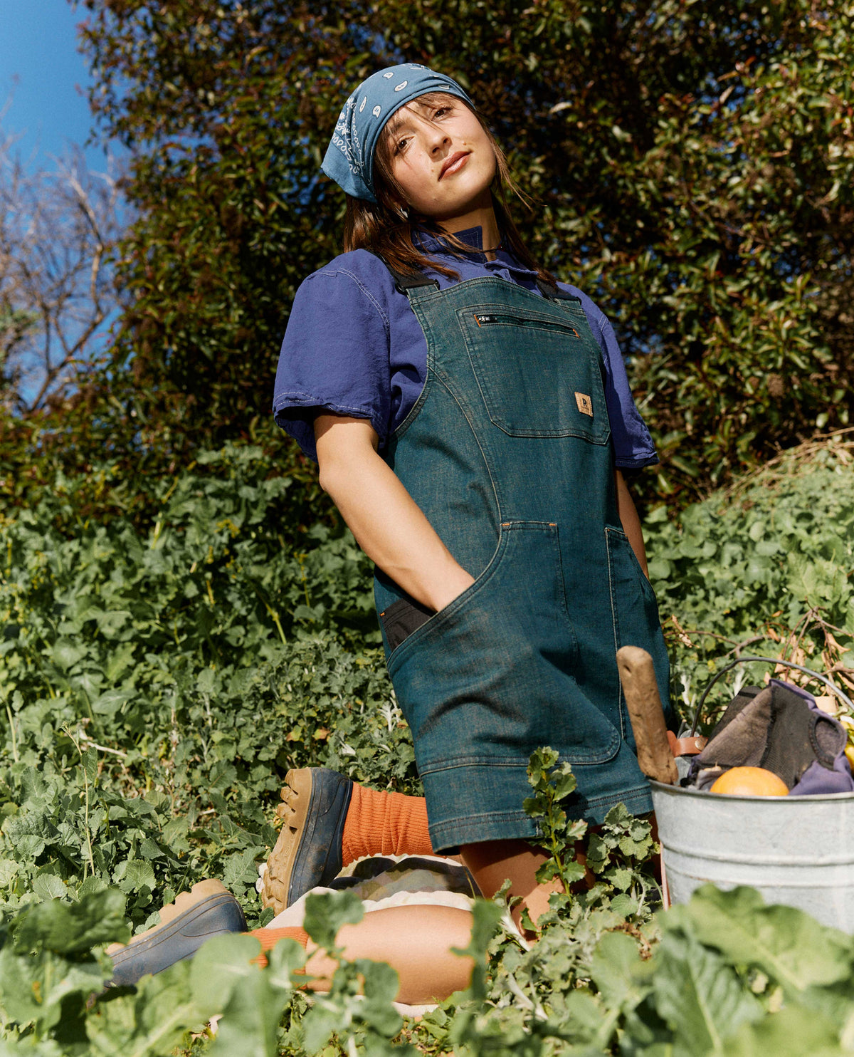 Person wearing a blue apron and hat in an outdoor garden setting