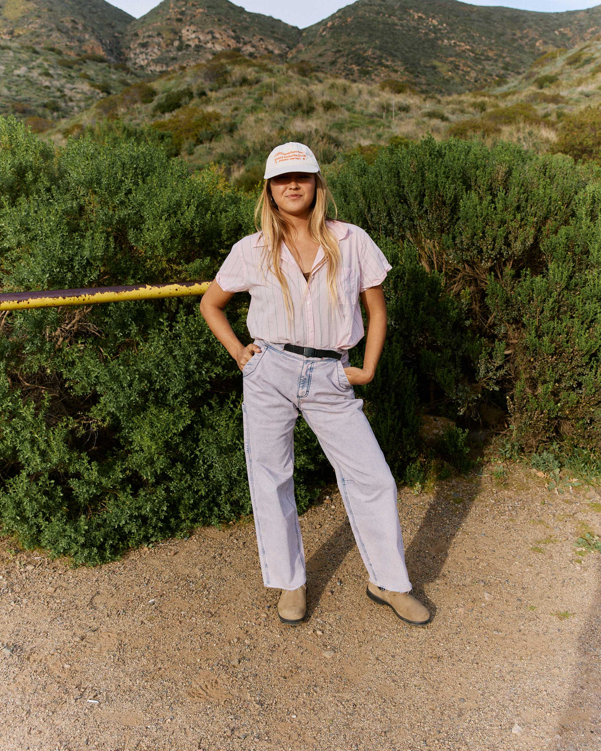 Person standing outdoors in a natural setting with mountains in the background