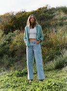 Woman standing in a grassy field wearing a green cardigan, white top, and light blue jeans.