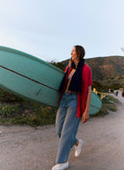 Woman walking with a teal kayak on her shoulder in a scenic outdoor setting.