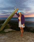 Woman holding a surfboard on a beach at sunset