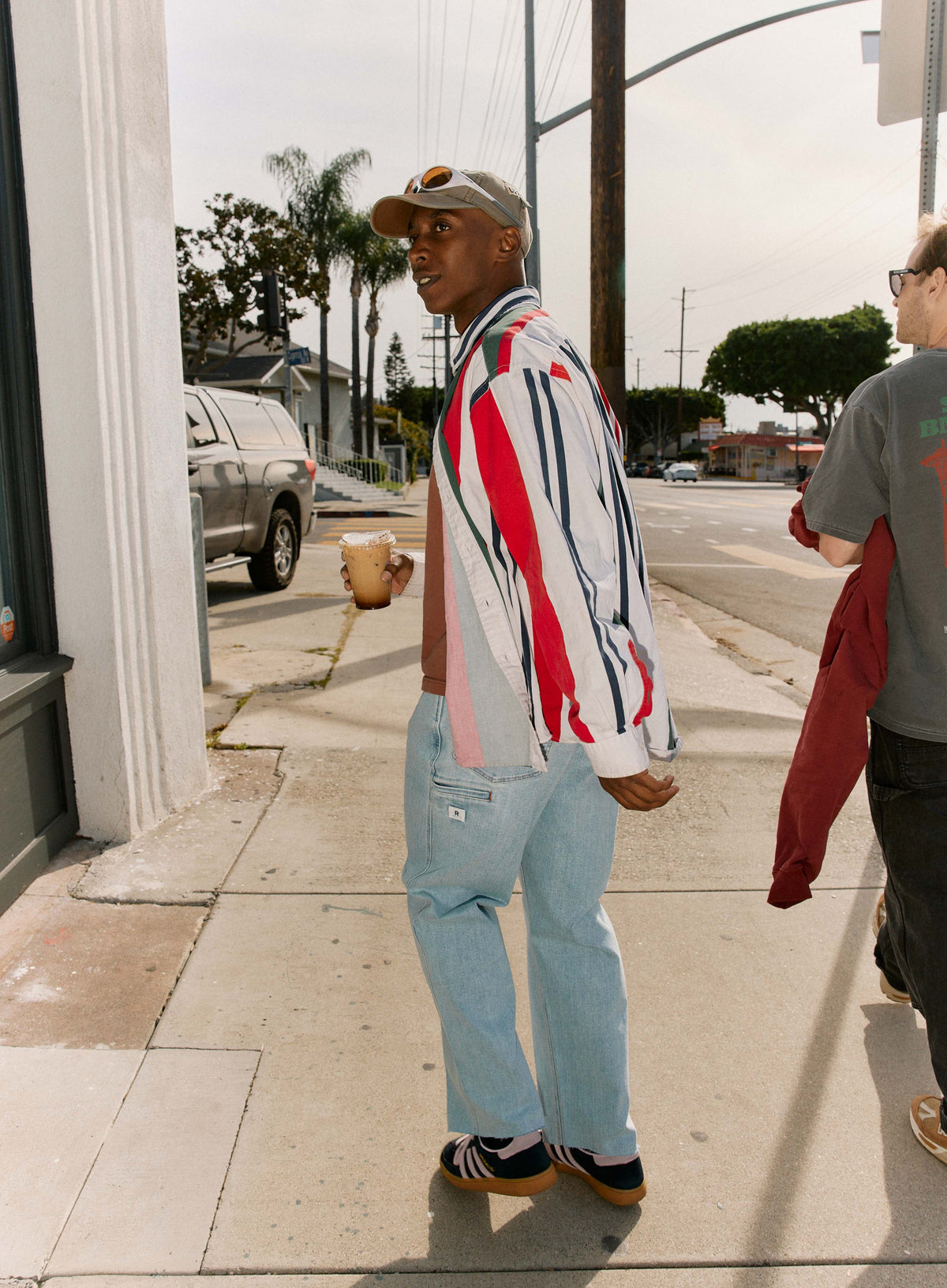 Man walking on a sidewalk wearing a colorful striped jacket and light blue jeans.