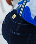 Close-up of a person wearing dark blue overalls with a visible brand logo, standing in a snowy landscape.