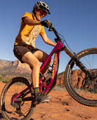Person riding a pink Santa Cruz mountain bike on a dirt trail with red rock formations in the background.