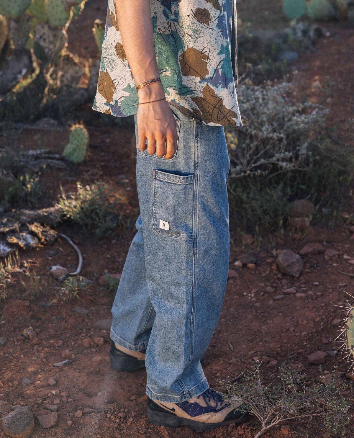 Man's legs in blue jeans with multi-color shirt standing in desert