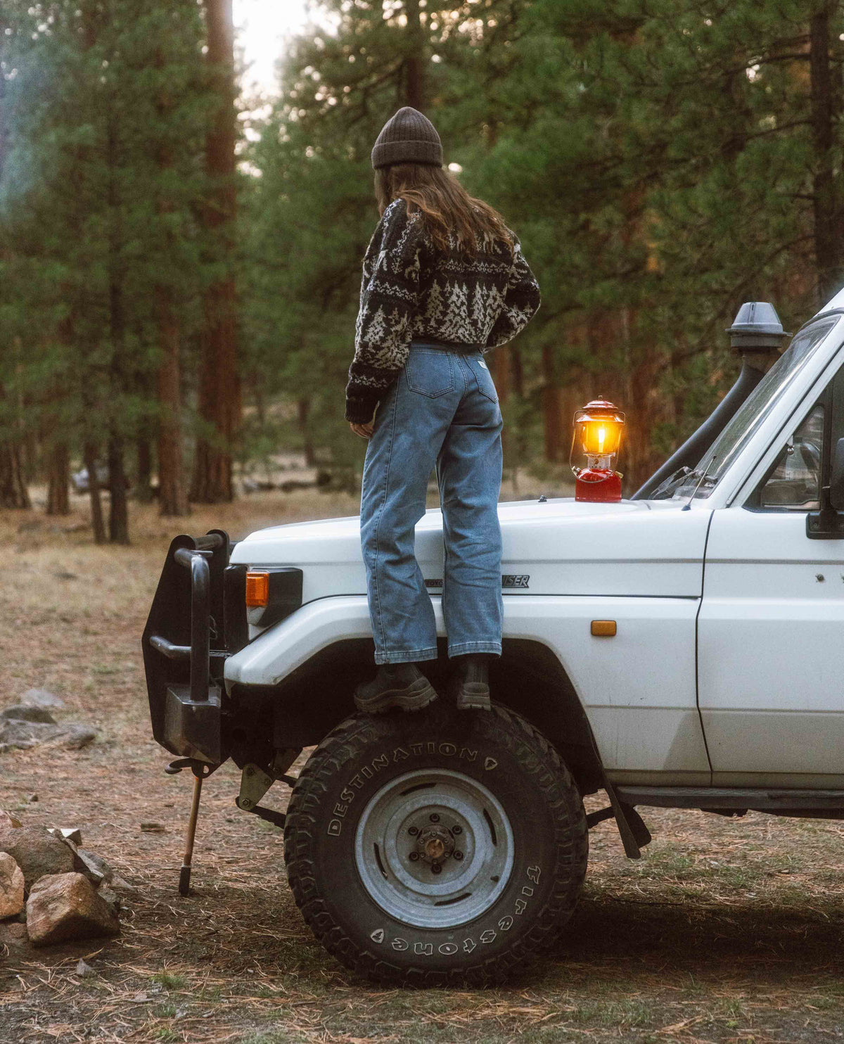 Person standing on a white SUV in a forest