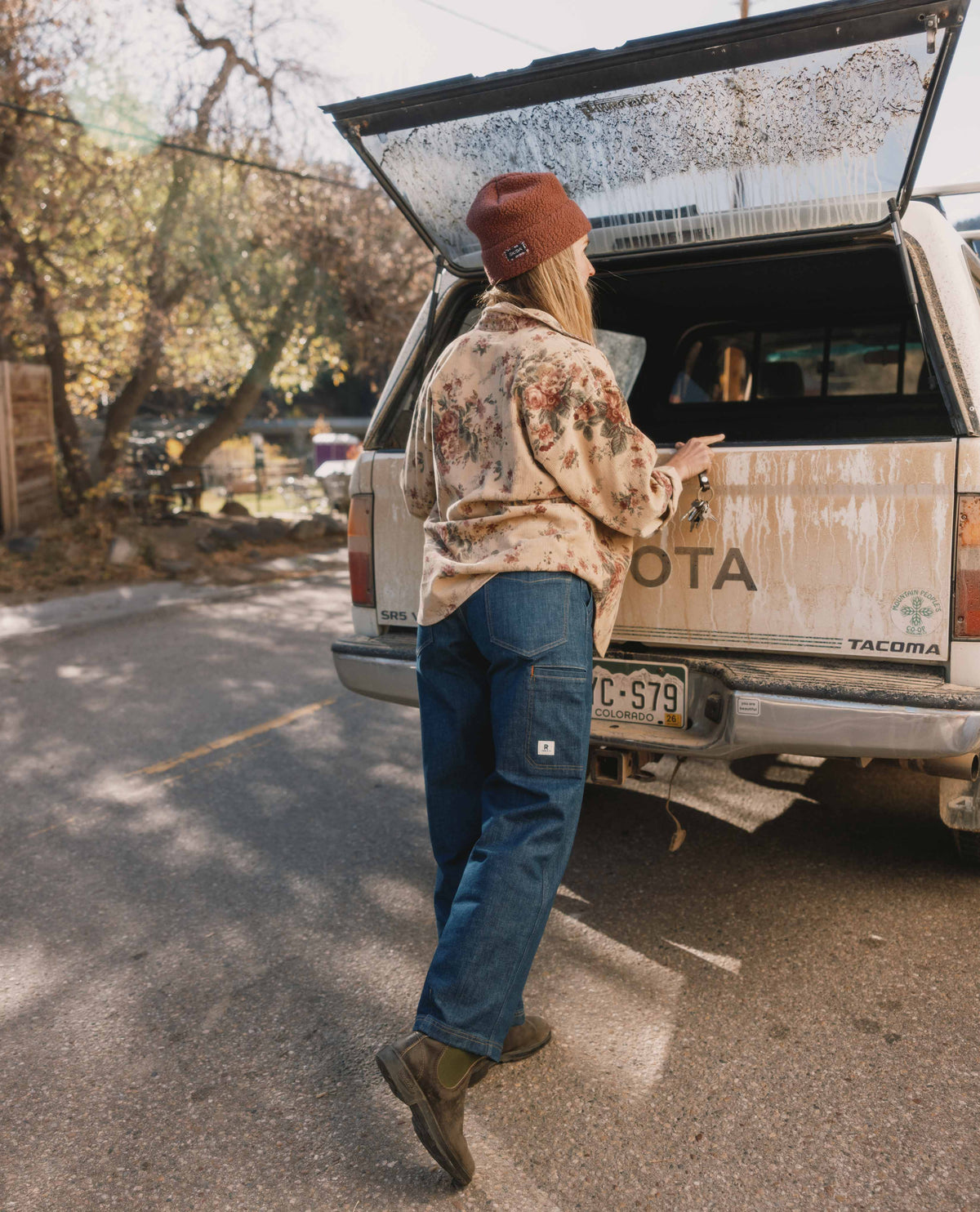 Person opening the trunk of a Toyota Tacoma truck on a road with trees in the background