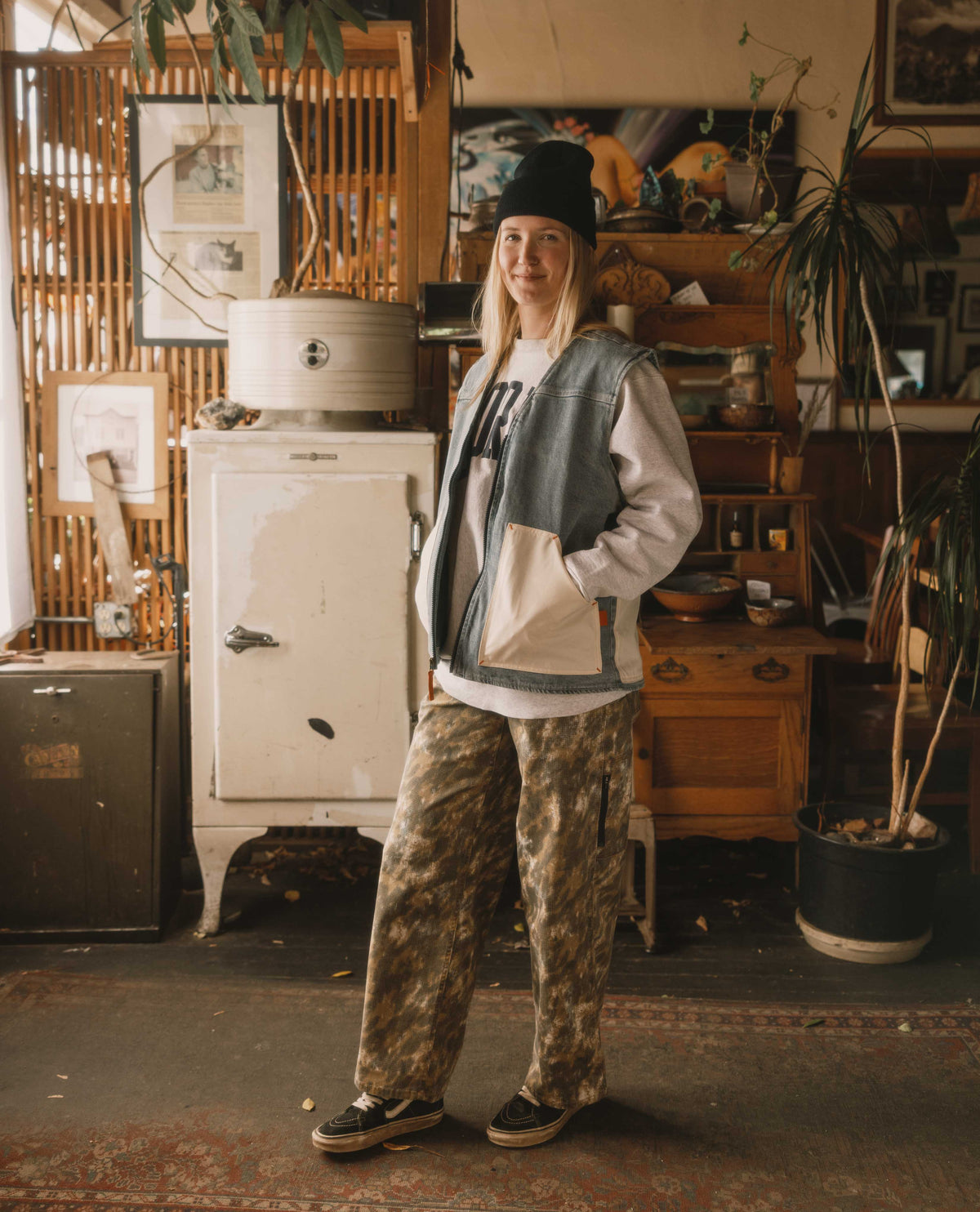 Person wearing a black hat and casual outfit standing in a room with vintage furniture and decor.