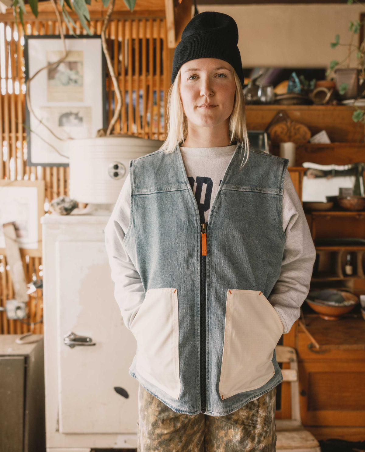 Person wearing a denim vest and black beanie in a rustic indoor setting