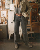 Person wearing a green jacket and dark jeans standing in a rustic indoor setting.