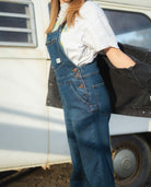Person wearing blue denim overalls standing next to a vintage vehicle.