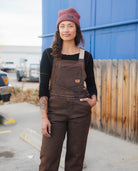 Person wearing brown overalls and a maroon beanie standing outdoors.