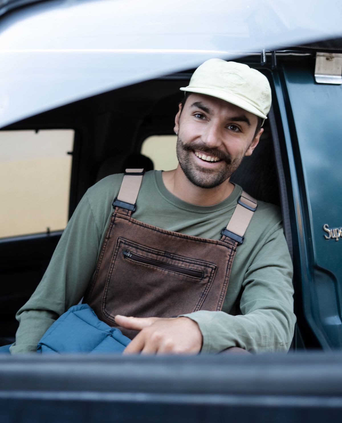 Man in overalls and cap sitting in a vehicle, smiling.