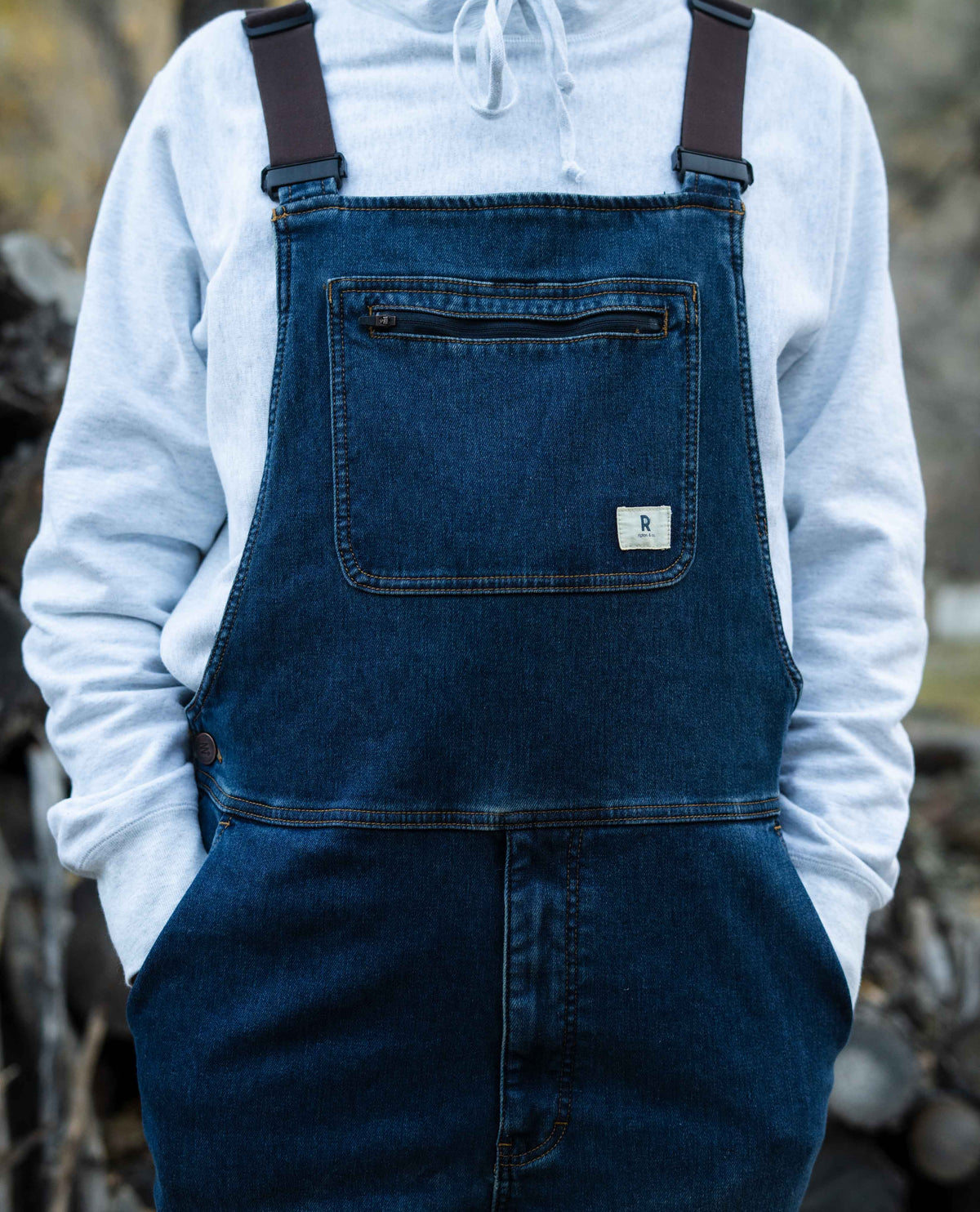 Person wearing a blue denim apron over a white hoodie with a blurred natural background