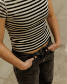Close up of woman wearing striped shirt with hands in pockets of gray pants 