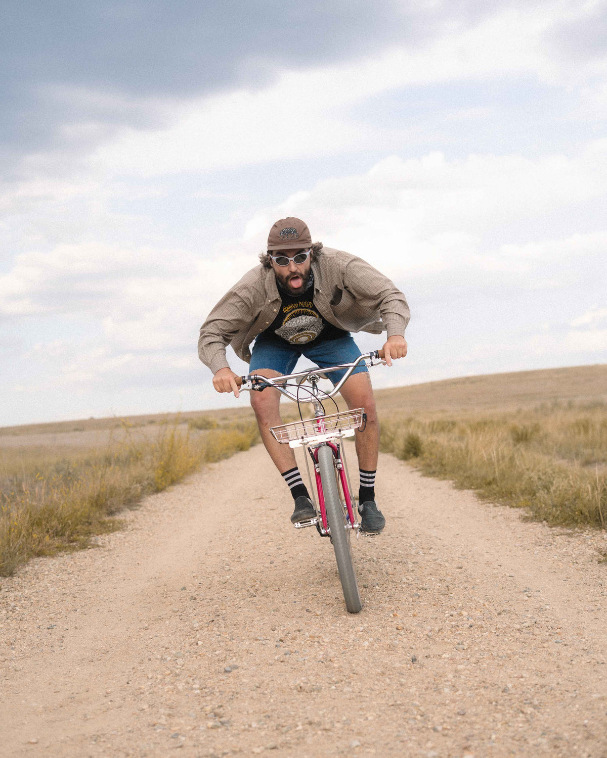 A man riding a red and white mountain bike on a dirt path in an open grassy landscape under a cloudy sky.