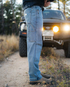Person wearing blue jeans standing on a dirt road with a vehicle in the background