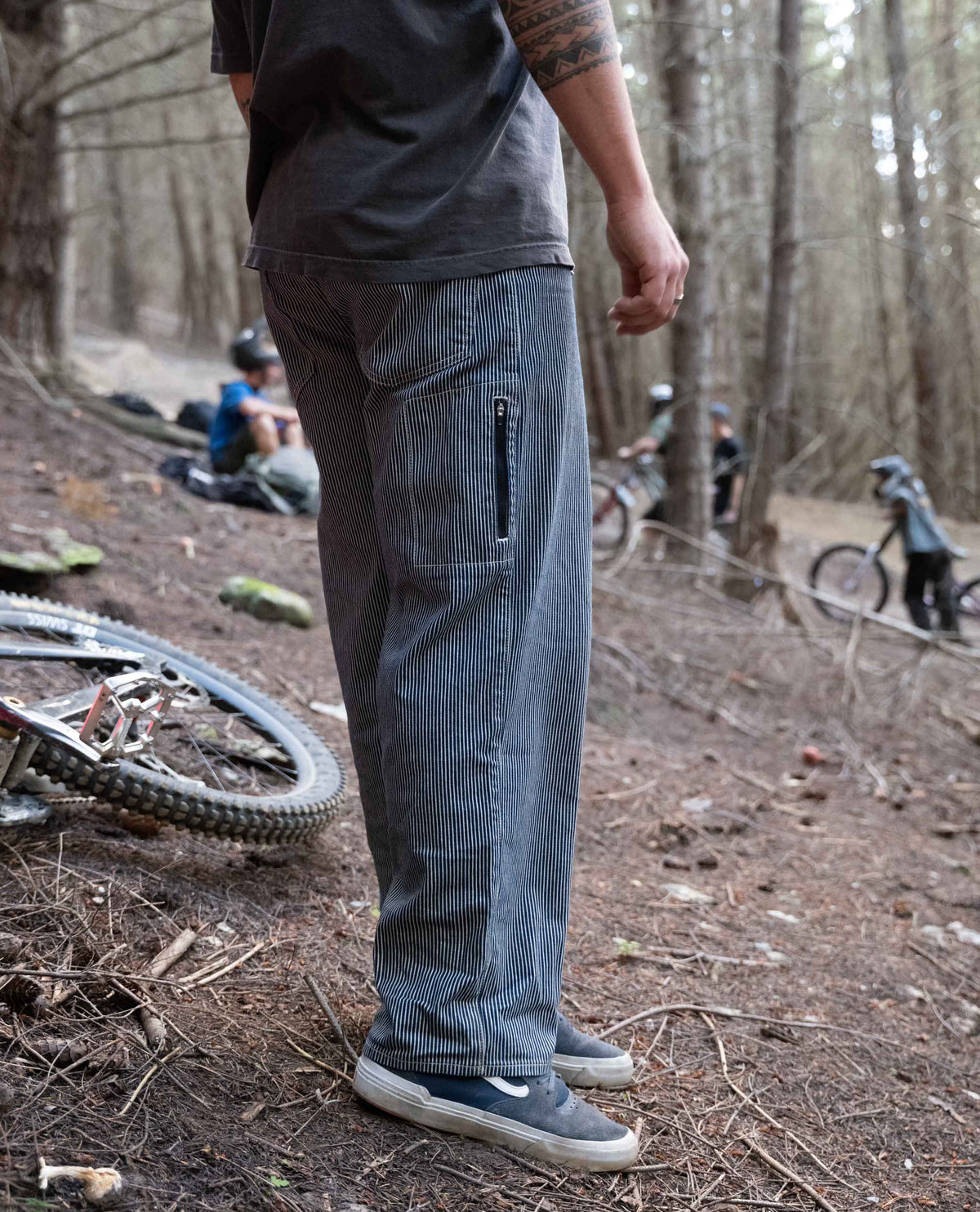Person wearing gray pants in a forest setting with bicycles and people in the background
