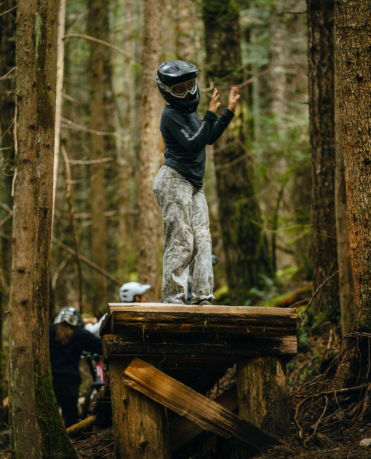 Person on a wooden platform in a forest wearing protective gear