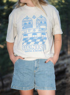 Close up of woman wearing blue shorts and white shirt outside, with hands in pockets 