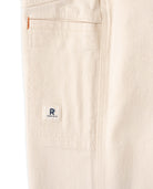 Close-up of beige pants with a brand logo on the pocket
