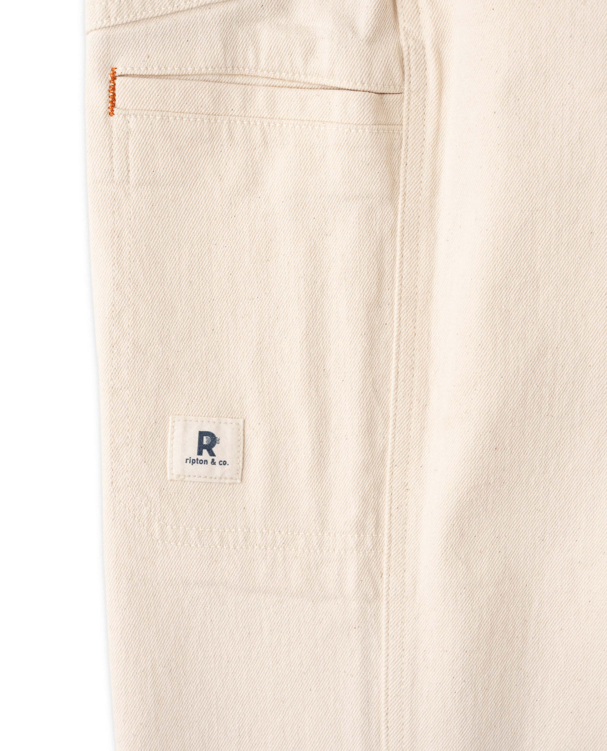 Close-up of beige pants with a brand logo on the pocket