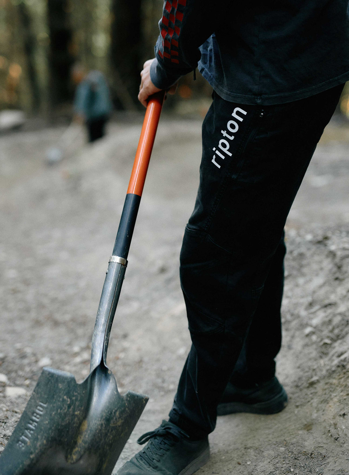 Person holding a shovel with 'ripton' branding on pants, blurred background