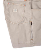 Close-up of beige pants with a brand logo on a white background