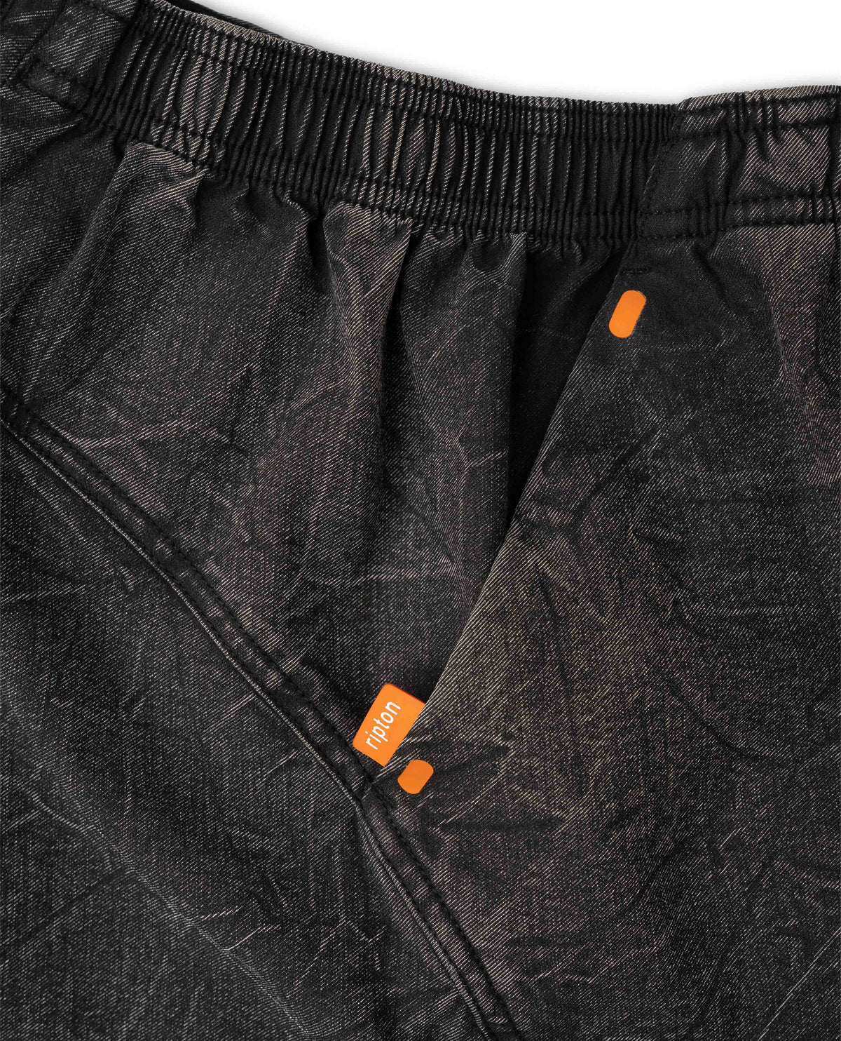 Close-up of black pants with orange accents and a brand logo on a white background