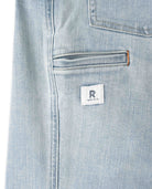 Close-up of light blue denim fabric with a brand label on a white background