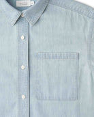 A close-up of a light blue chambray button-down shirt with a collar, white buttons, and a chest pocket. The brand label 'Ripton & co.