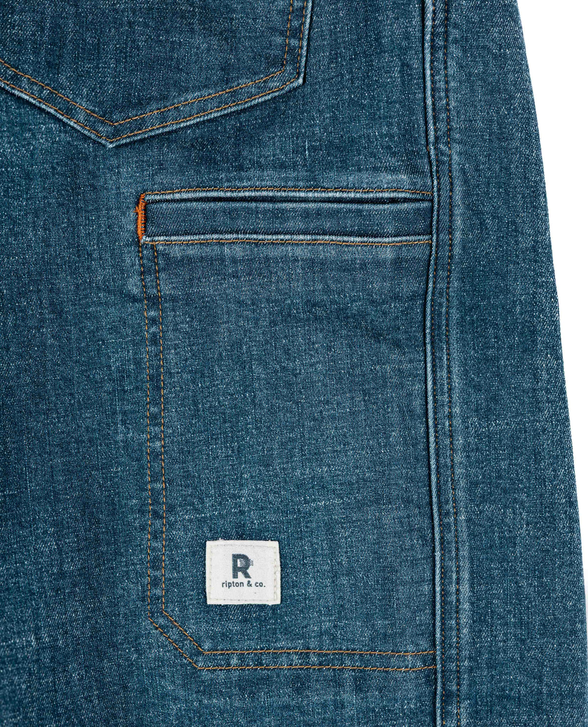 Close-up of a blue denim pocket with a brand label on a white background