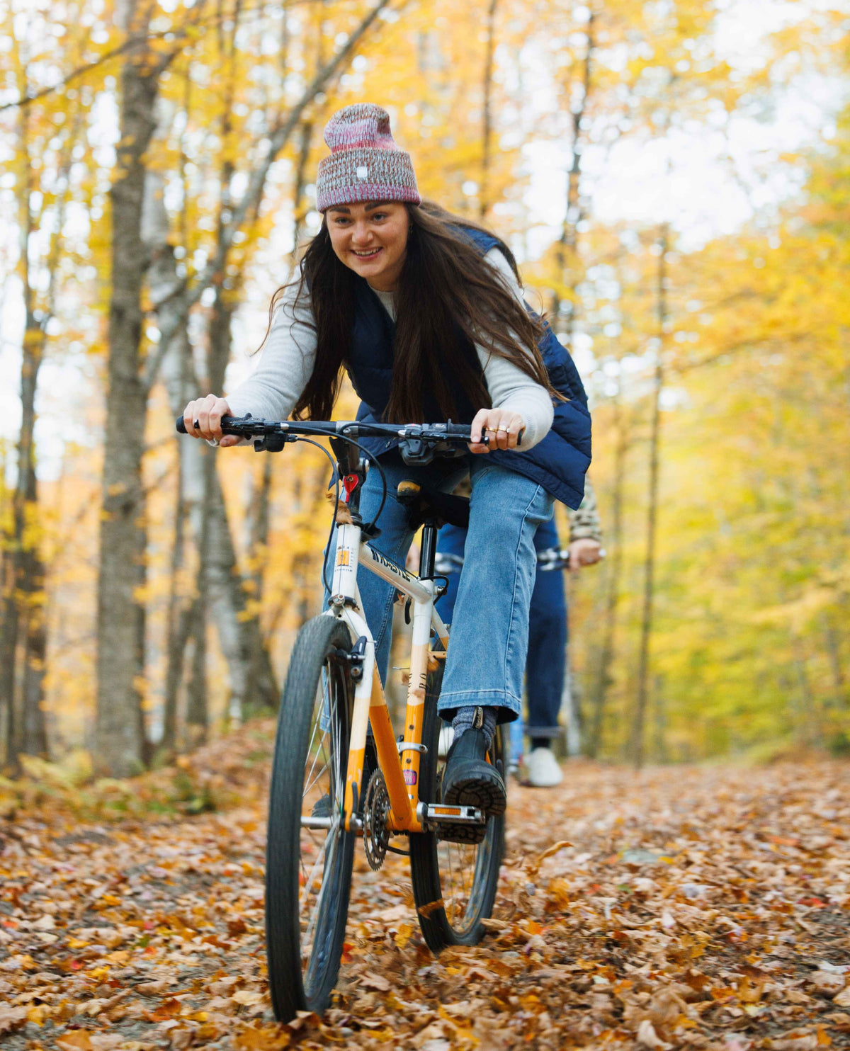 Woman riding a bicycle through a forest with autumn leaves