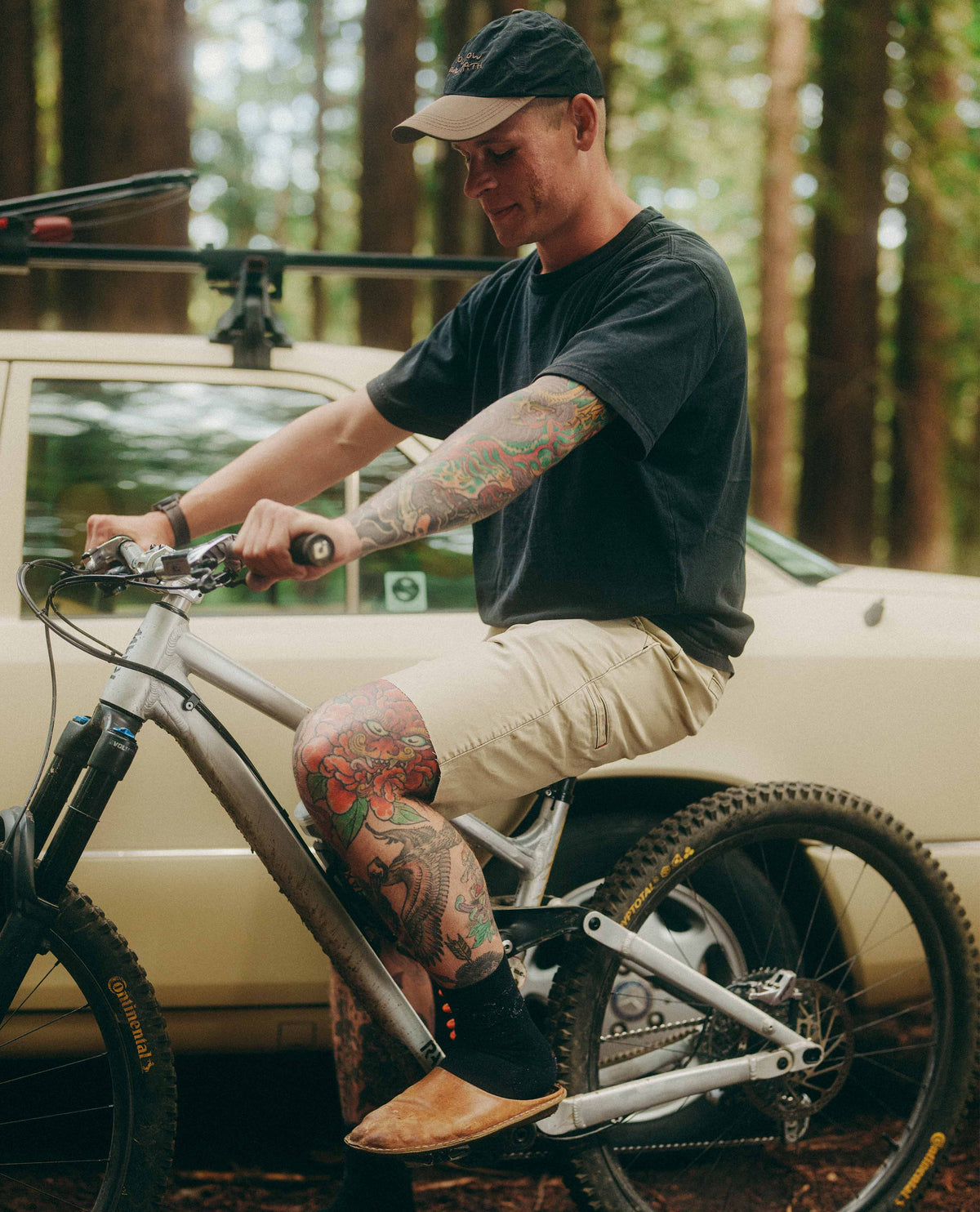 Man with tattoos sitting on a bicycle in a forested area