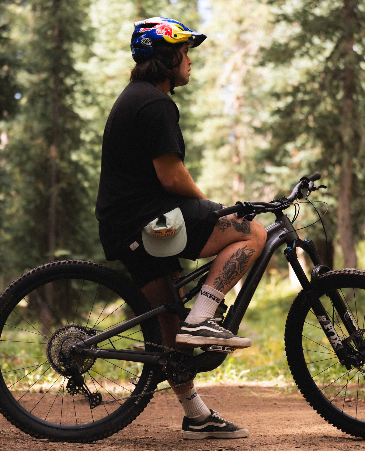 Man sitting on bike with blue helmet, black clothes, outside in the woods 