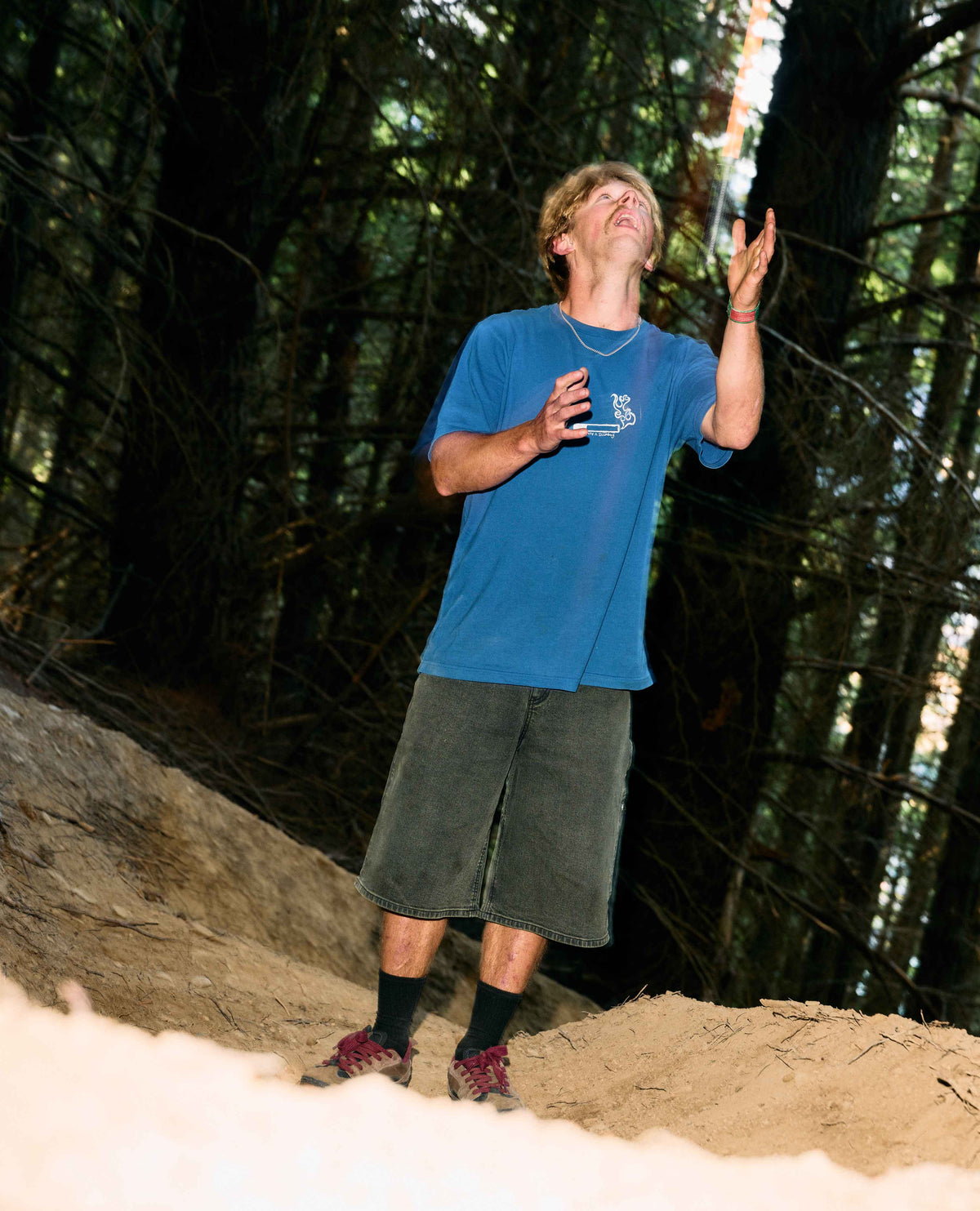Person in a blue shirt and shorts standing on a dirt path with trees in the background