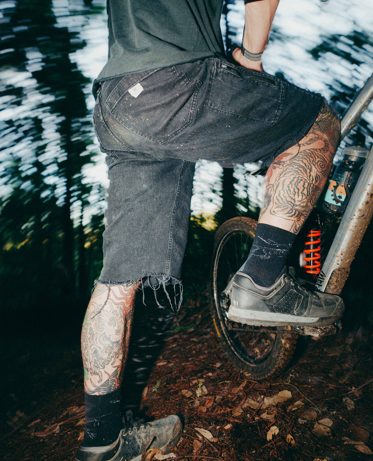 Person with tattoos riding a unicycle in a forest setting
