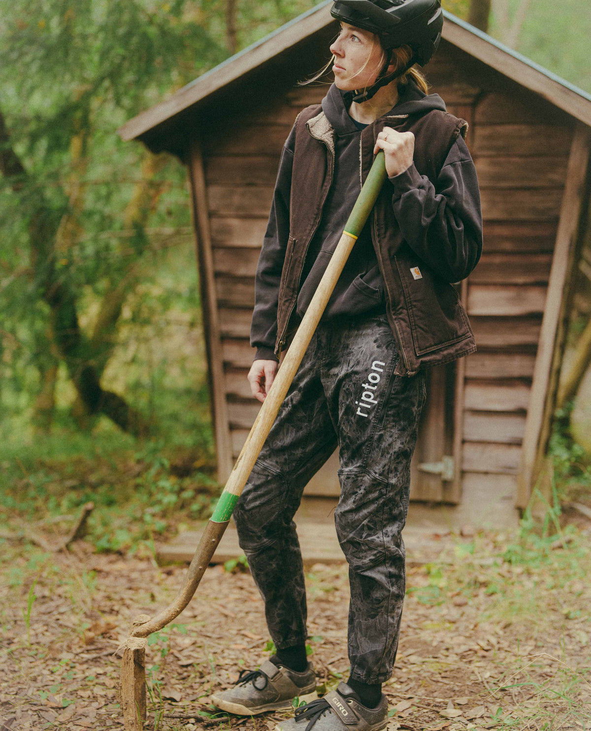 Person in outdoor setting holding a long tool, wearing a helmet and dark jacket.